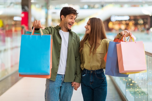 Pareja emocionada mostrando coloridos bolsos de compras en el centro comercial