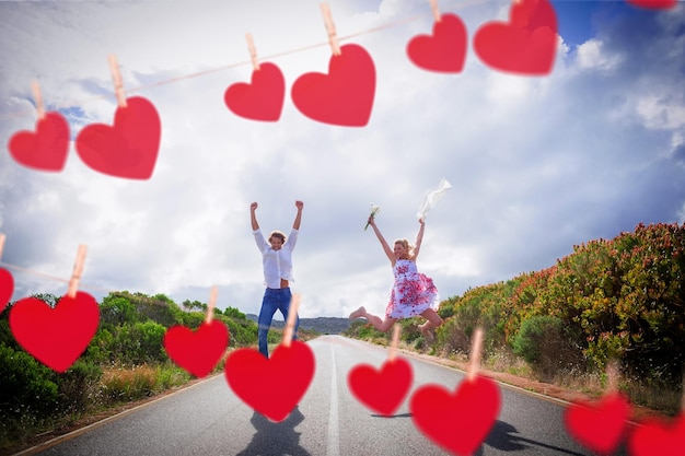 Pareja emocionada saltando en la carretera contra corazones colgando de una línea