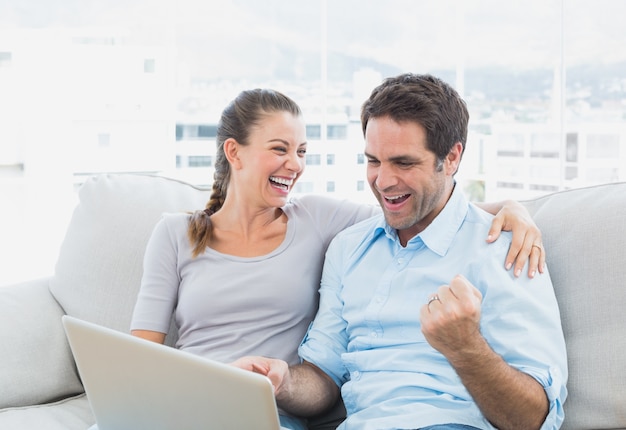 Foto pareja emocionada sentado en el sofá usando la computadora portátil juntos