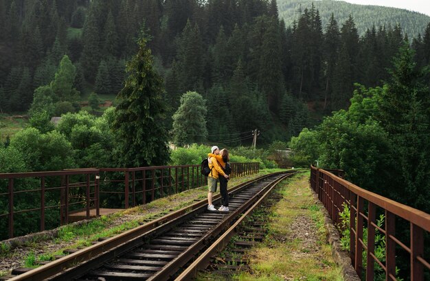 Pareja enamorada abrazándose y besándose en un puente ferroviario en las montañas de pie en la vía