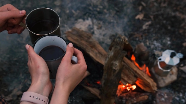 Pareja enamorada Camping con pozo de fuego y dos tazas de hojalata con té caliente café Fogata ardiente