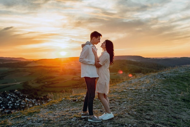 Una pareja enamorada, un chico y una chica están parados en una montaña al atardecer abrazándose y besándose