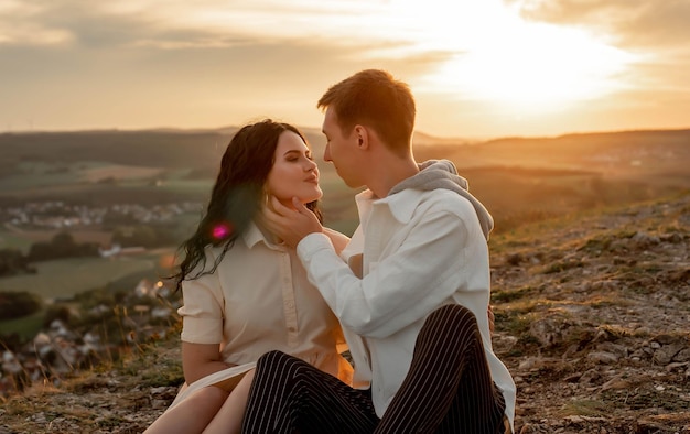 pareja enamorada, un chico y una chica están sentados en una montaña al atardecer besándose y abrazándose