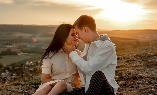 pareja enamorada, un chico y una chica están sentados en una montaña al atardecer besándose y abrazándose