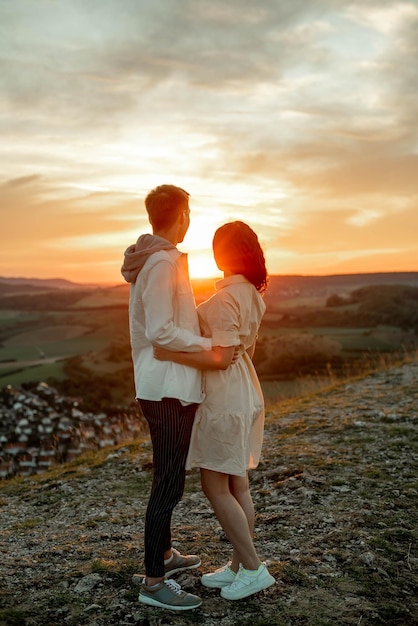 pareja enamorada, un chico y una chica se paran en una montaña al atardecer y miran la puesta de sol