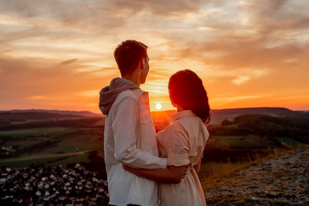 pareja enamorada, un chico y una chica se paran en una montaña al atardecer y miran la puesta de sol