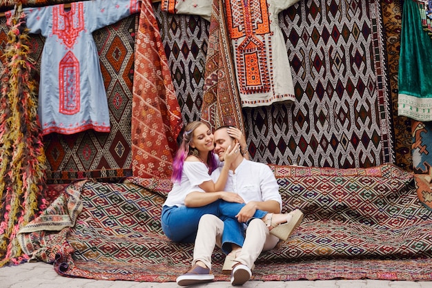 Pareja enamorada compra una alfombra y textiles hechos a mano en un mercado oriental en Turquía. Abrazos y caras alegres y felices de hombres y mujeres.