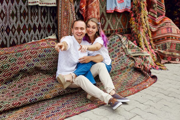 Pareja enamorada compra una alfombra y textiles hechos a mano en un mercado oriental en Turquía. Abrazos y caras alegres y felices de hombres y mujeres.