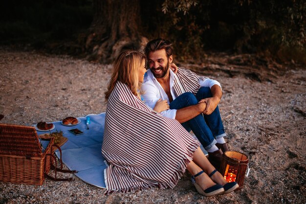 Pareja enamorada cubierta de manta disfrutando juntos de un picnic