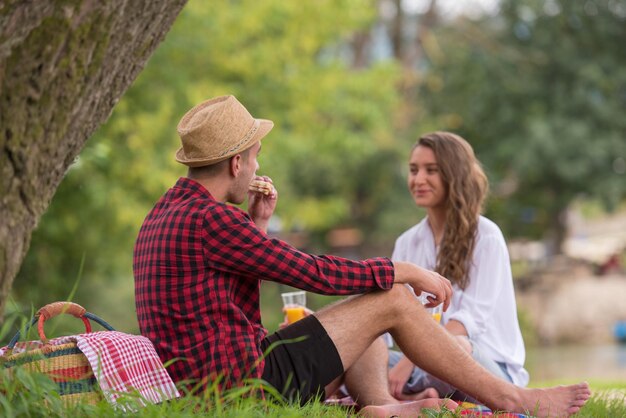 Pareja enamorada disfrutando de la comida y la bebida de la hora del picnic en la hermosa naturaleza en la orilla del río