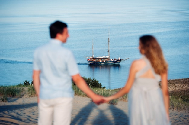 Una pareja enamorada se encuentra en la playa de las dunas con el telón de fondo del mar Báltico y un barco