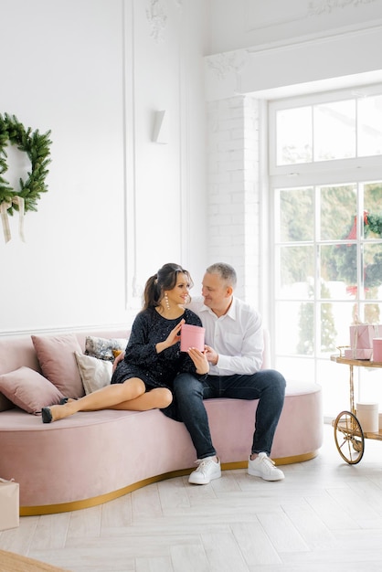 Una pareja enamorada está sentada en el sofá de la sala de estar y dándose regalos de Navidad