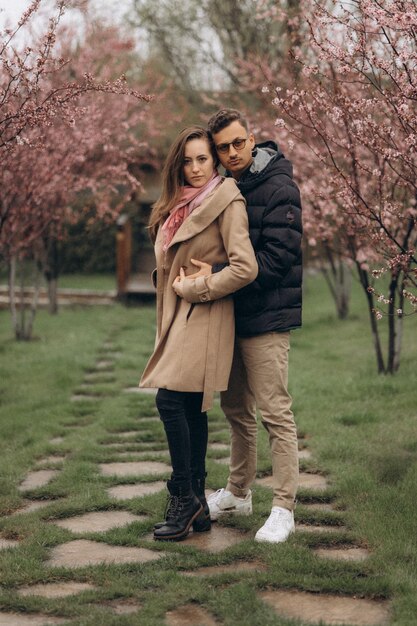 Una pareja enamorada parada en un camino frente a cerezos rosados.