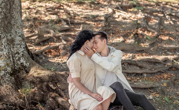 Una pareja enamorada, una pareja y una chica se sientan bajo un hermoso árbol y se acarician, se besan