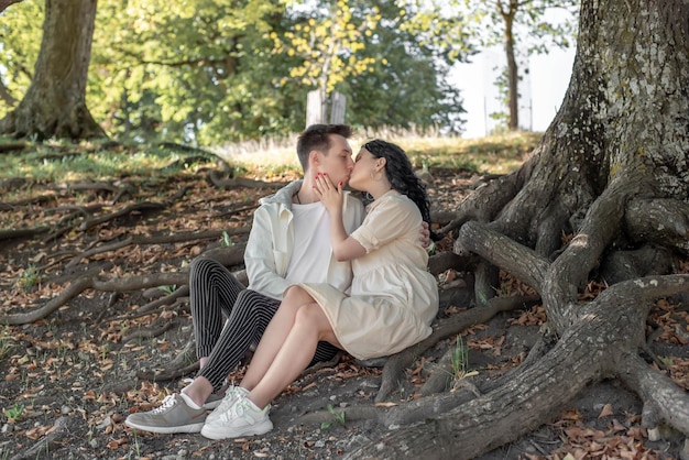 Una pareja enamorada, una pareja y una chica se sientan bajo un hermoso árbol y se acarician, se besan