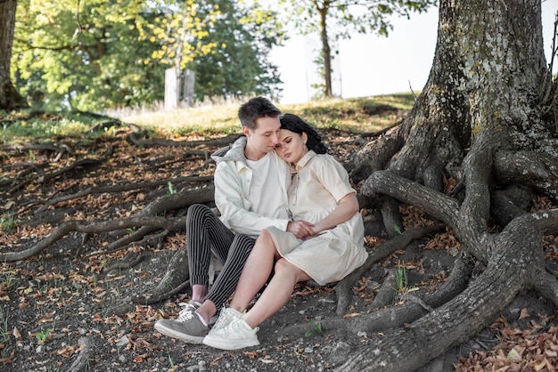 Una pareja enamorada, una pareja y una chica se sientan bajo un hermoso árbol y se acarician, se besan