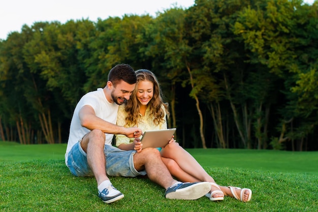 Pareja enamorada relajándose en el parque chico y chica juegan juegos en la comunicación de la tableta en el inter...