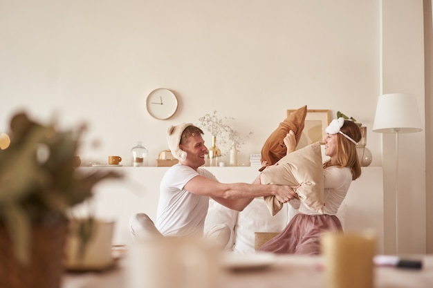 Pareja enamorada riendo y jugando en la cama. Hombre y mujer luchan almohadas. Joven pareja feliz golpeó las almohadas en la cama en una habitación en casa