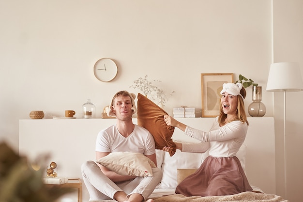 Pareja enamorada riendo y jugando en la cama. Joven pareja feliz golpeó las almohadas en la cama en una habitación en casa