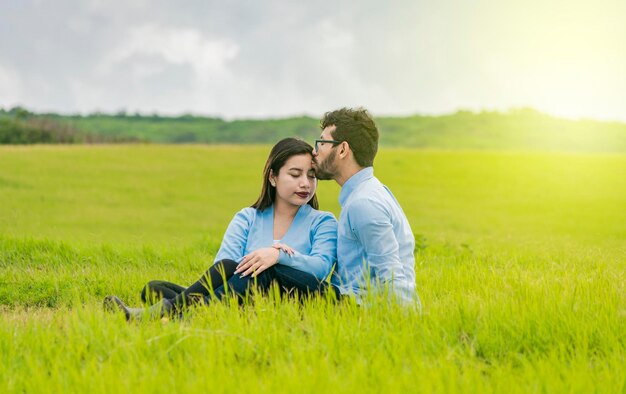 Una pareja enamorada sentada en el campo besándose la frente Un hombre besando la frente de su novia en el campo Pareja romántica sentada en el césped besándose la frente