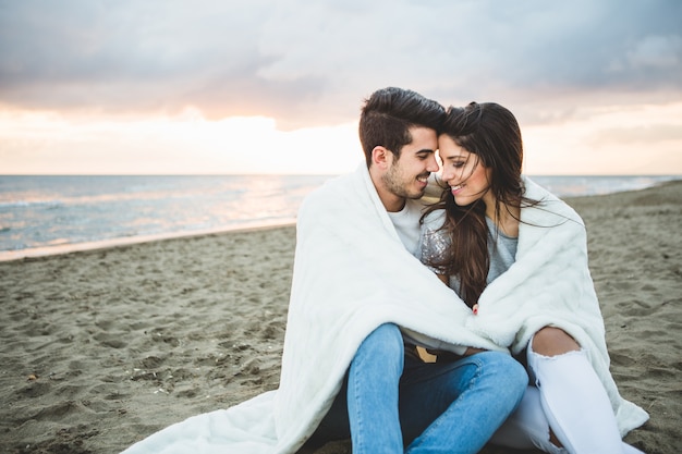 Foto pareja enamorada sentada en una playa cubierta por una manta blanca