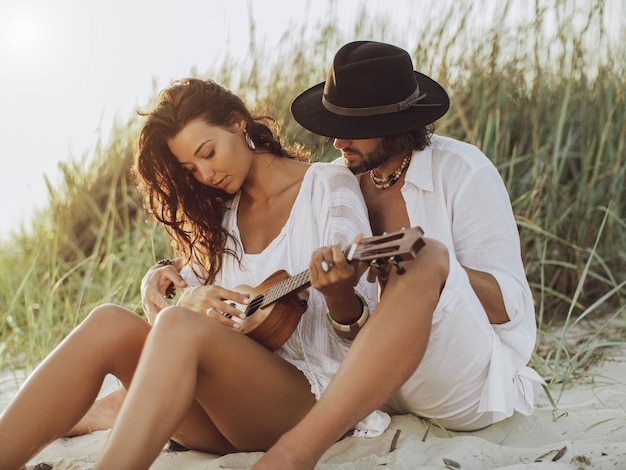 Pareja enamorada tocando la guitarra y descansando en la playa