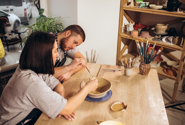 Pareja enamorada trabajando juntos en rueda de alfarero en taller de estudio artesanal