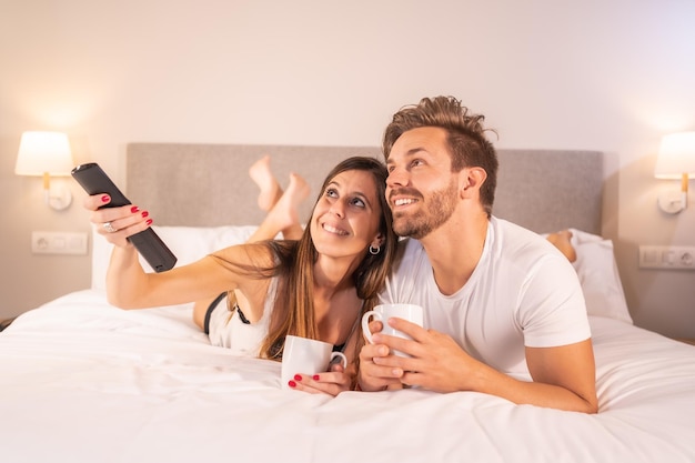 Una pareja enamorada viendo la televisión encima de la cama del hotel en pijama