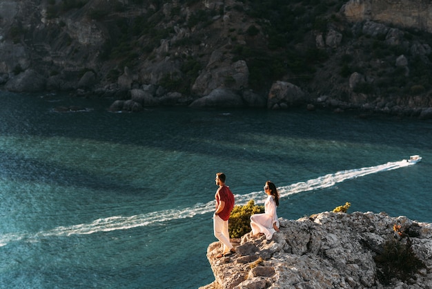 Pareja de enamorados al amanecer junto al mar. Luna de miel. Hombre y mujer se encuentran con la puesta de sol junto al mar. Hombre y mujer viajando. Viajes de boda. Romance de vacaciones. Hermosa pareja junto al mar. Copia espacio