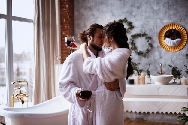 pareja de enamorados en albornoces con copas de vino en el baño. relajarse