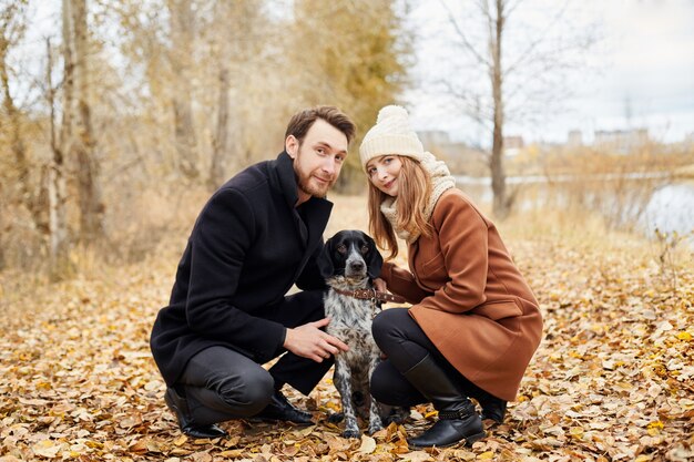 Pareja de enamorados en un cálido día de otoño camina en el parque con un alegre perro Spaniel