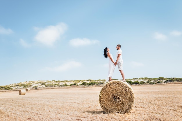 Pareja de enamorados en el campo. Hombre y mujer cerca de un pajar. Pajar redondo. Un hombre y una mujer de pie cerca de un pajar. Pareja viaja. Luna de miel. Pareja de recién casados. Hombre y mujer, manos de valor en cartera