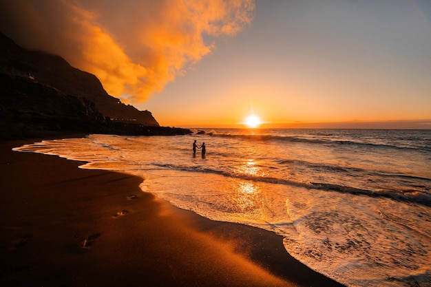 Una pareja de enamorados se encuentra en el océano por la noche mirando la hermosa puesta de sol en la isla de Tenerife. España.