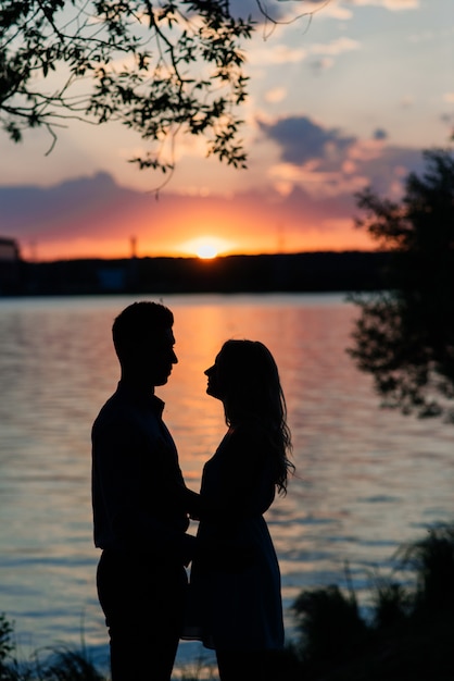 Pareja de enamorados retroiluminada silueta al atardecer lago naranja