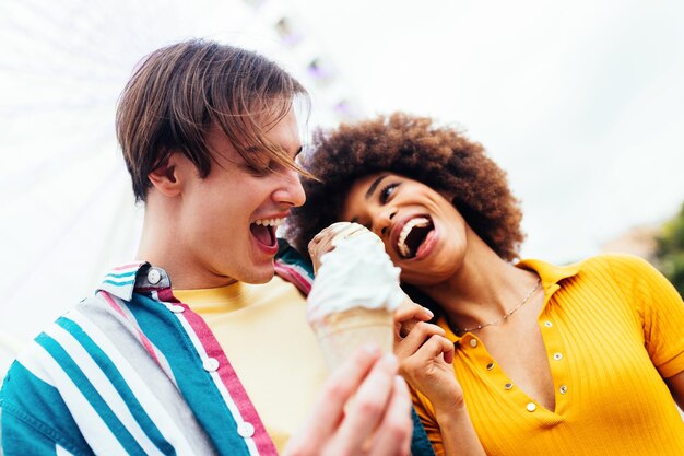 Foto pareja de enamorados saliendo en un parque de diversiones y comiendo helados