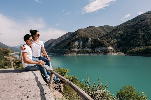 Foto pareja de enamorados sentados y mirando una hermosa vista del embalse de zhinvalskoe, georgia.