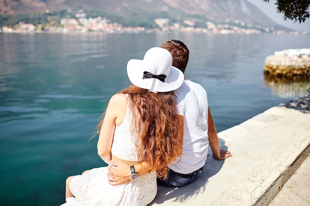 Pareja de enamorados sentados en el muelle cerca del mar. Hombre joven y mujer abrazándose. Día soleado de verano