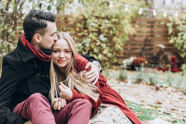 Pareja de enamorados sentados en otoño las hojas caídas en un parque, disfrutando de un hermoso día de otoño. Hombre besando a una mujer en la frente