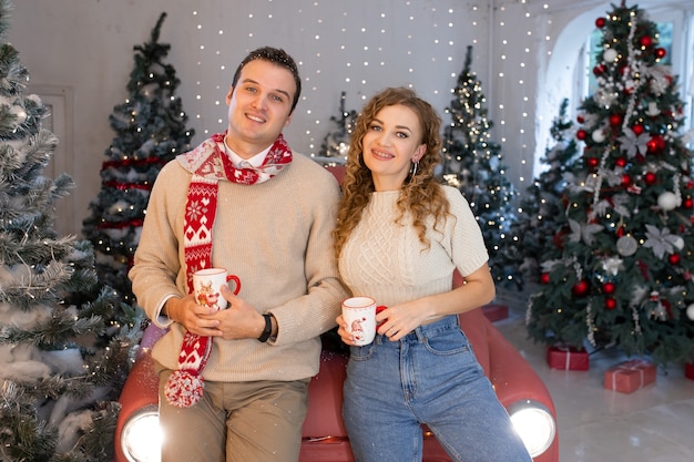 Pareja de enamorados sonriendo cerca del árbol de Navidad muy bien decorado, disfrutando de la magia navideña.