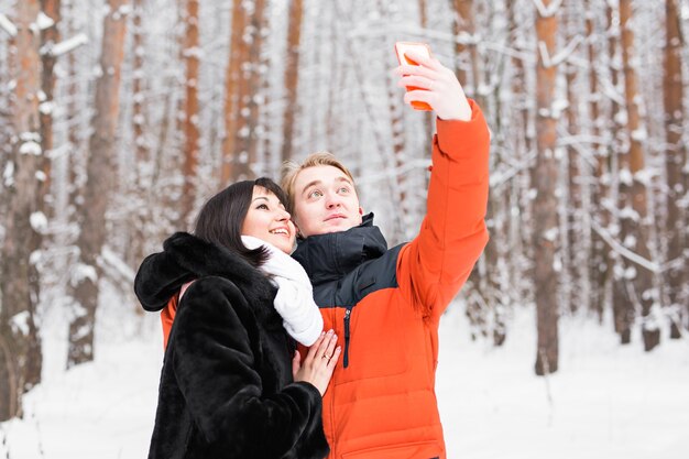 Pareja de enamorados sonriendo y haciendo selfie en invierno al aire libre.