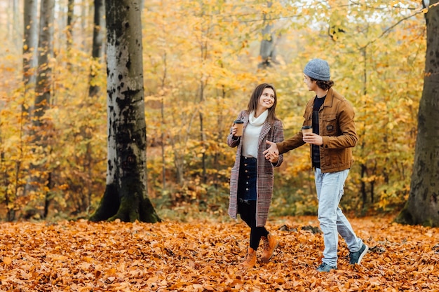 Pareja de enamorados sosteniendo tazas de té o café y caminando.