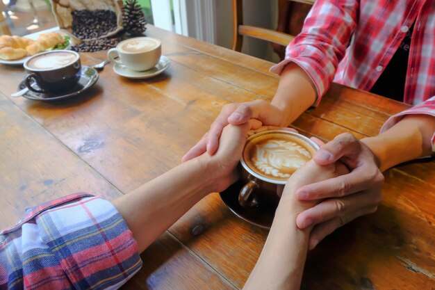 Pareja de enamorados tomados de la mano con café en la mesa de madera.