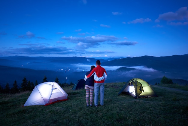 La pareja se encuentra cerca del campamento, de espaldas a la cámara, abrazándose