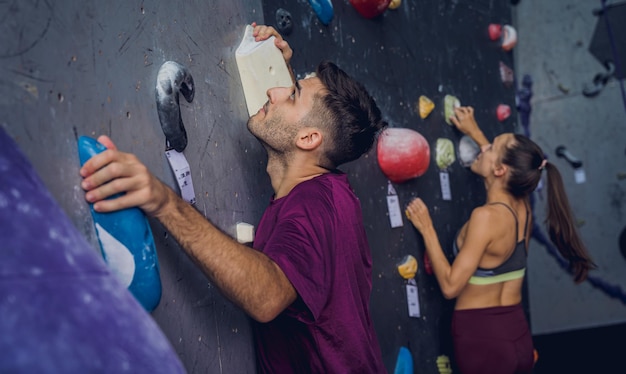Una pareja de escaladores fuertes suben a una pared artificial con garras y cuerdas de colores