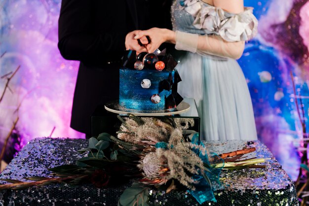 Pareja espacial cortó un pastel de bodas decorado con chocolate y planetas. El concepto de postres festivos para las vacaciones.