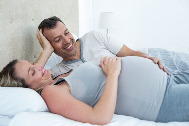 Pareja esperando acostada en la cama y charlando en su dormitorio