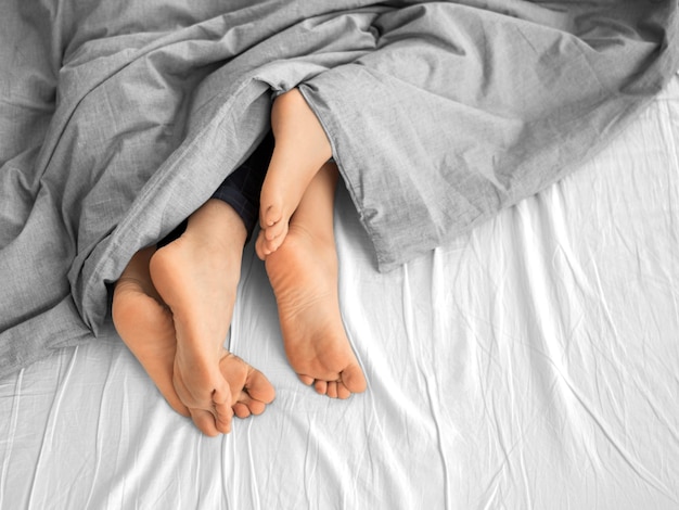 La pareja está durmiendo un primer plano de las piernas que sobresalen de debajo de la manta