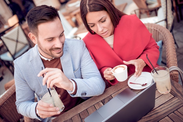 La pareja está sentada en el café y usando una computadora portátil