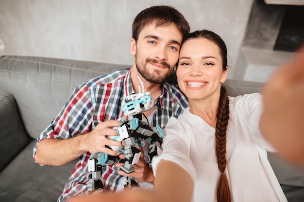 Pareja está sentada en el sofá y haciendo selfie con un robot.