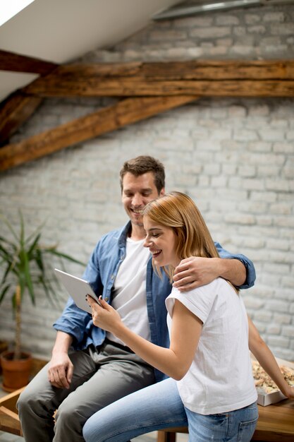 La pareja está usando una tableta digital y sonriendo mientras está sentada en la mesa en casa